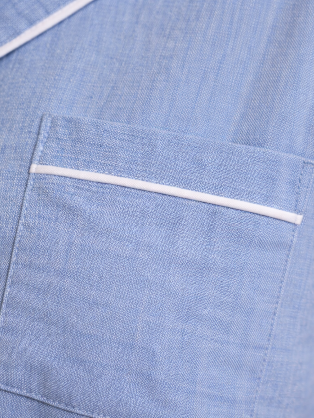 Close-up of a light blue textured fabric garment with a pocket and a thin white piping accent.
