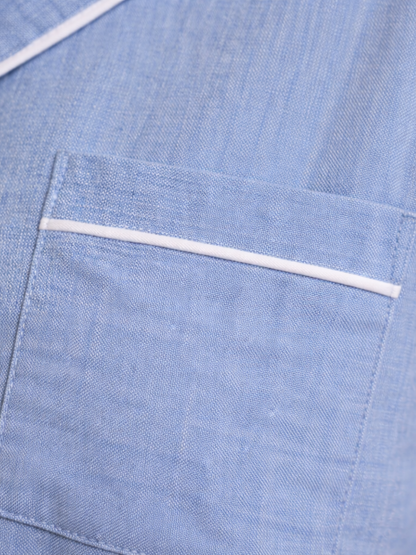 Close-up of a light blue textured fabric garment with a pocket and a thin white piping accent.