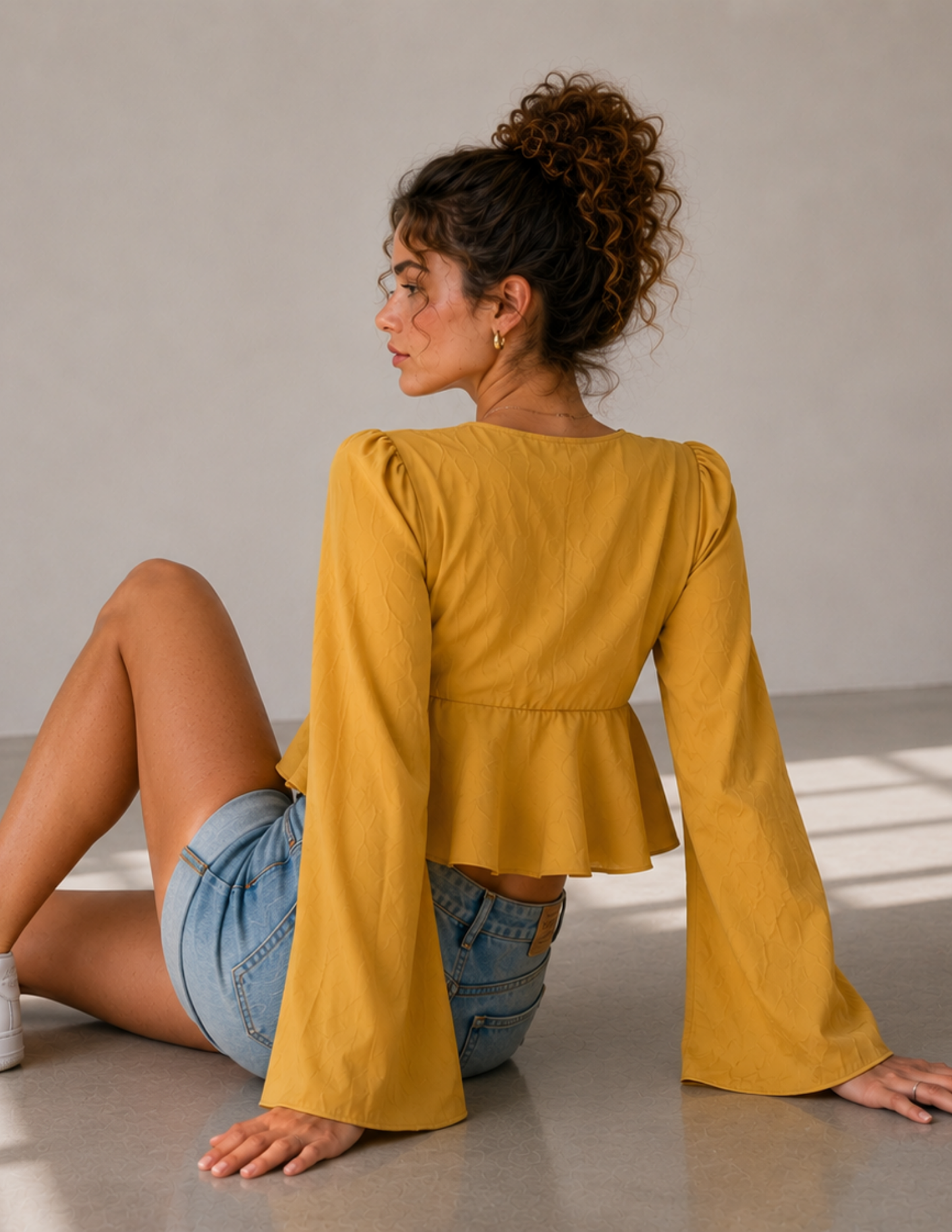 Back view of the MARBELLA women’s peplum top sewing pattern, showing the gathered waist, flared peplum and long wide sleeves in textured mustard yellow fabric