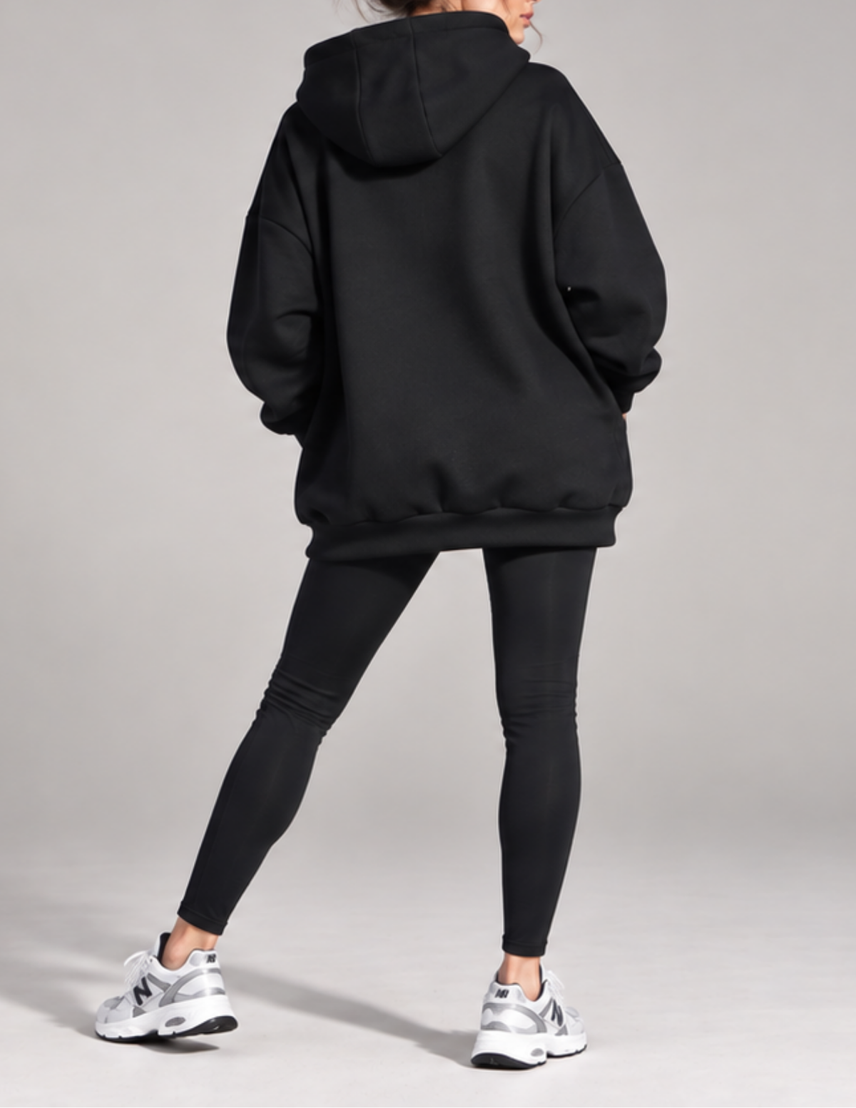 A person shown from the back wearing an oversized black hoodie, black leggings, and white New Balance sneakers against a light gray studio background.
Back view of the Melani women's 
oversized hoodie showing the 
relaxed silhouette, spacious hood, 
dropped shoulders, voluminous 
sleeves and ribbed bottom band 
extending below the hips.