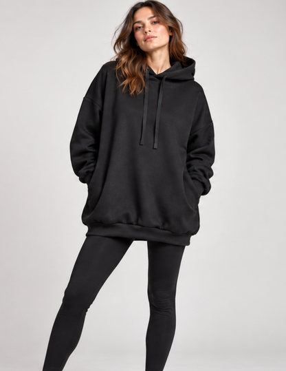A woman modeling an oversized black pullover hoodie with matching black leggings against a light gray studio background.
Front view of a woman wearing the 
Melani oversized black hoodie with a 
spacious drawstring hood, long 
voluminous sleeves, ribbed cuffs, 
ribbed hem and relaxed below-hip 
fit