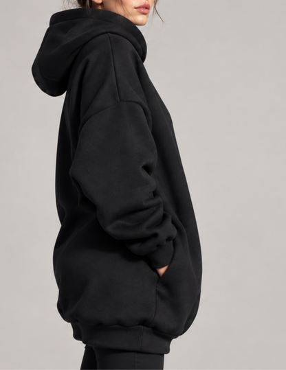 A person shown in side profile wearing an oversized black pullover hoodie against a plain light gray studio background.
Side view of the Melani oversized 
black hoodie showing the spacious 
hood, dropped shoulder, voluminous 
sleeve, ribbed cuff and practical 
angled side pocket