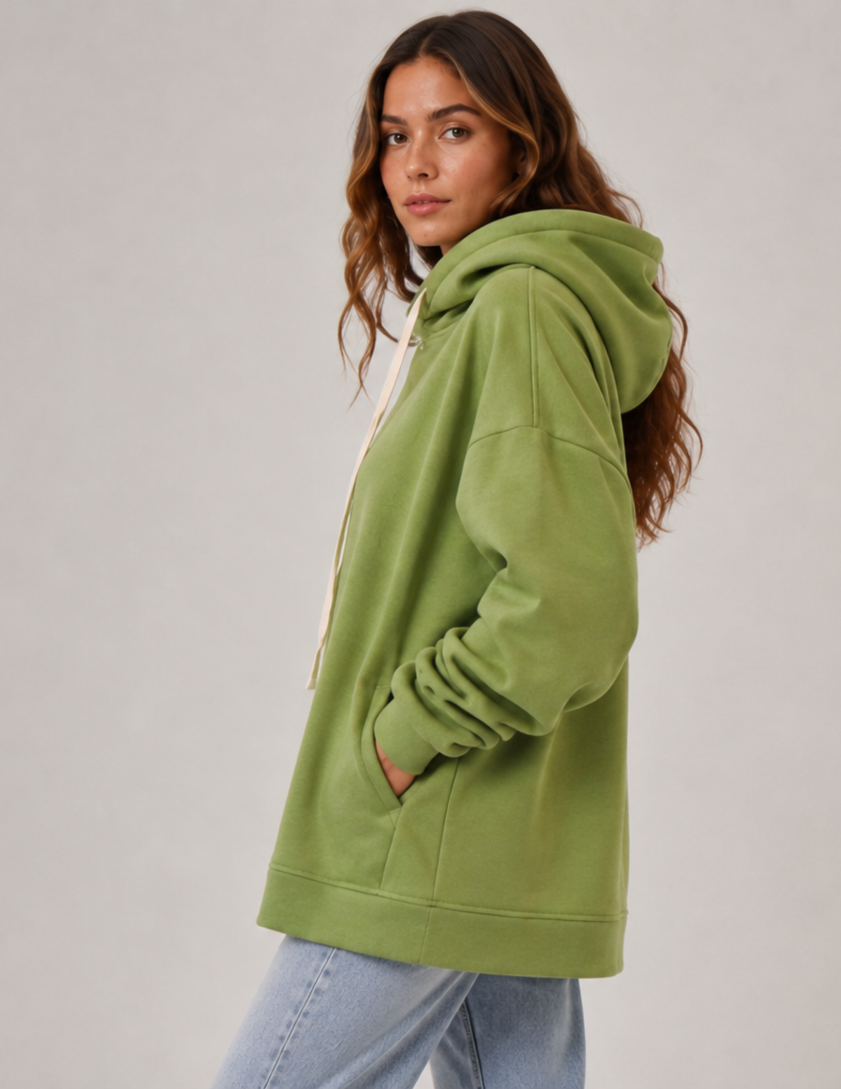 Side view of a woman wearing the OLEA relaxed fit hoodie with a large hood, dropped shoulder, long sleeve and integrated pocket